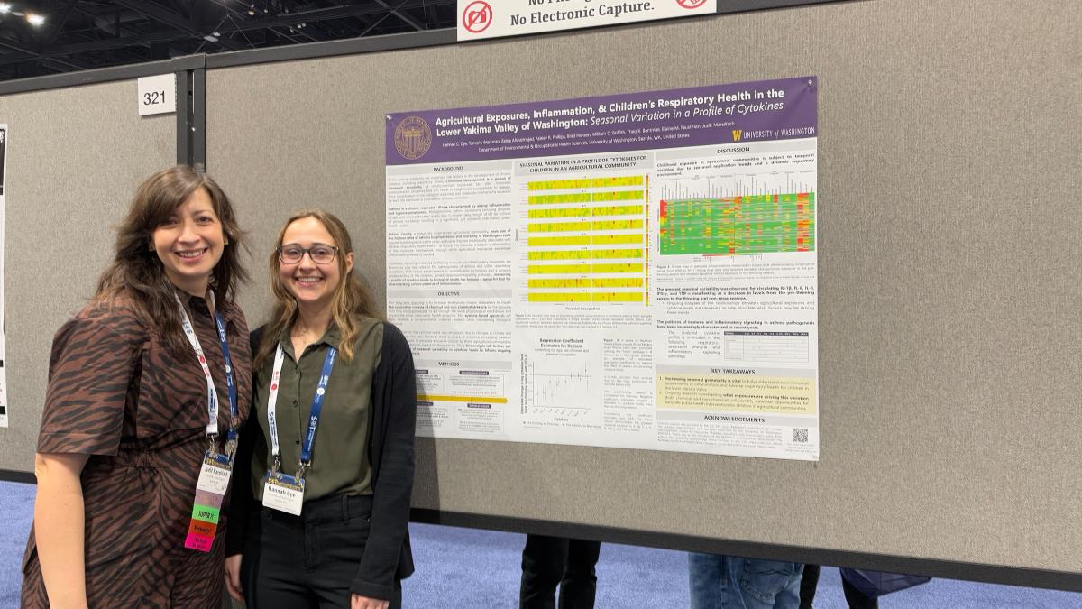 Judit Marsillach and Hannah Dye stand together in front of a research poster.