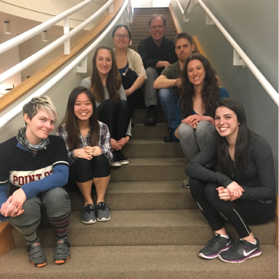 Eight people sit on an indoor staircase smiling. 