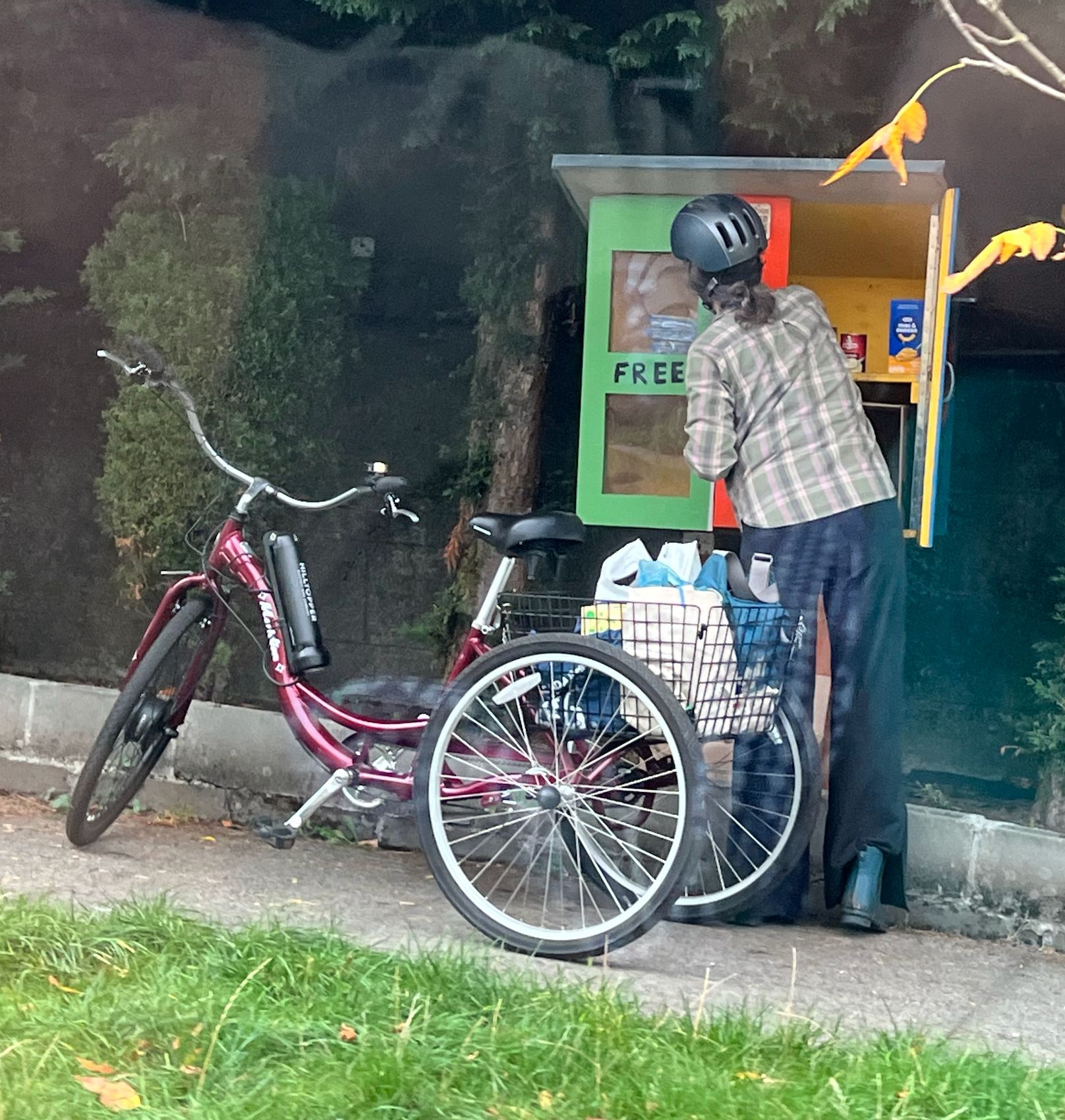 A person facing away from the camera, wearing a bike helmet, is reaching into an open micropantry. There are two bicycles parked in the foreground.