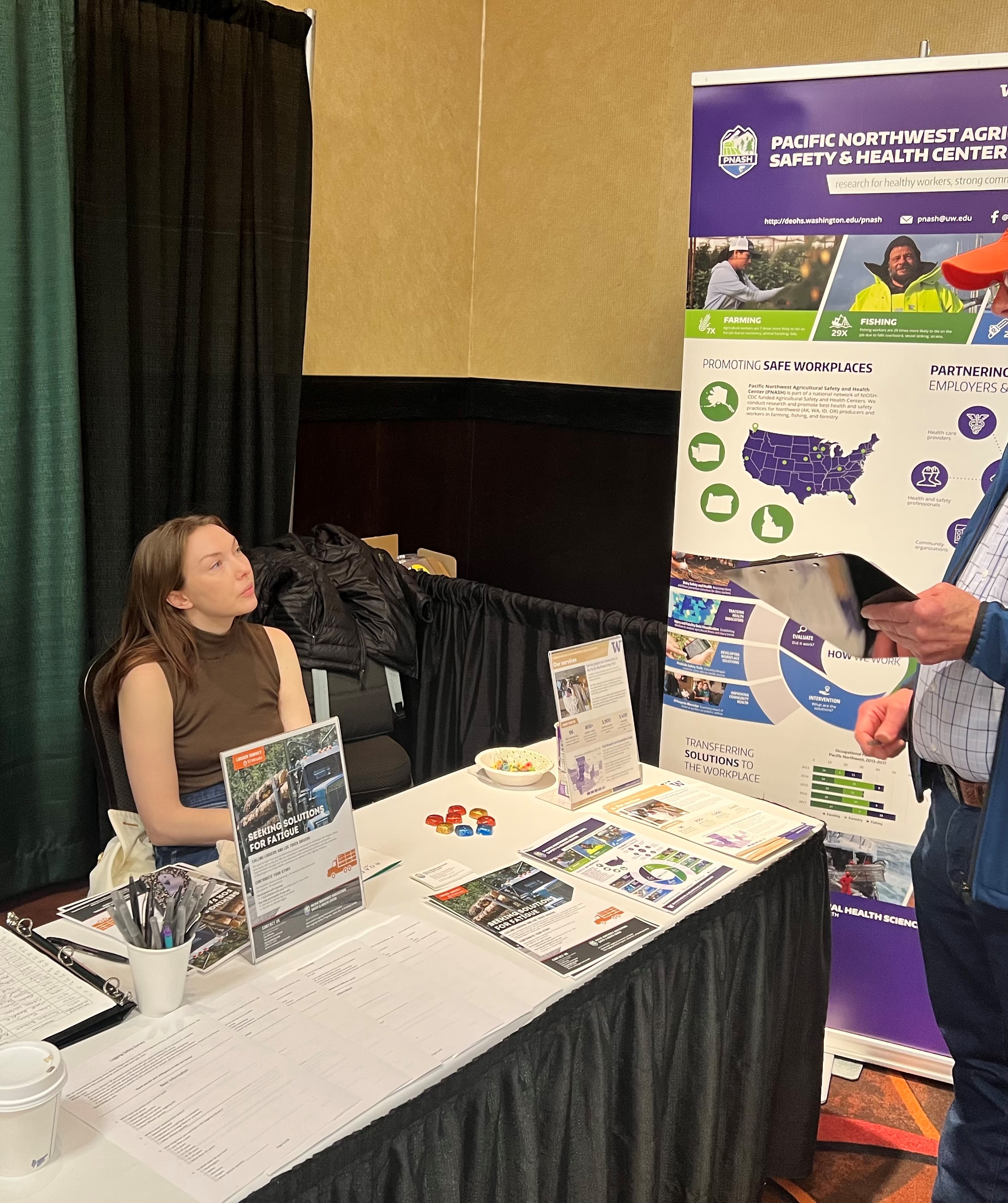 Woman with auburn hair in sleeveless brown top sits at table with research materials.