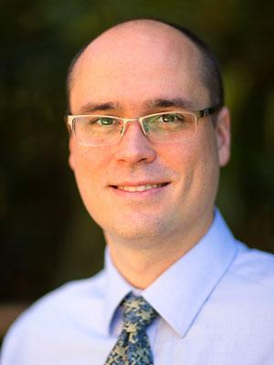 Dr Beck, a middle-aged bald white man with gold glasses in a nice shirt and tie