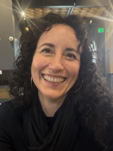 Woman with long curly brown hair wearing a black top