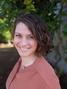 Woman with curly brown hair wearing coral top