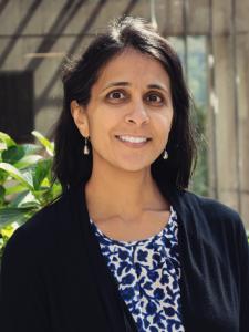 Woman with black hair and black sweater over a blue and white patterned shirt.