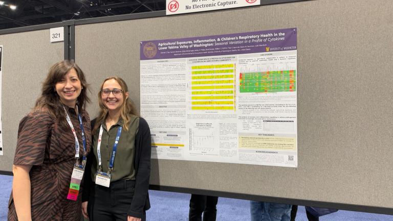 Judit Marsillach and Hannah Dye stand together in front of a research poster.