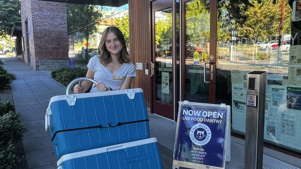 Woman with light brown hair pushes a dolly loaded with blue coolers to the UW Food Pantry.